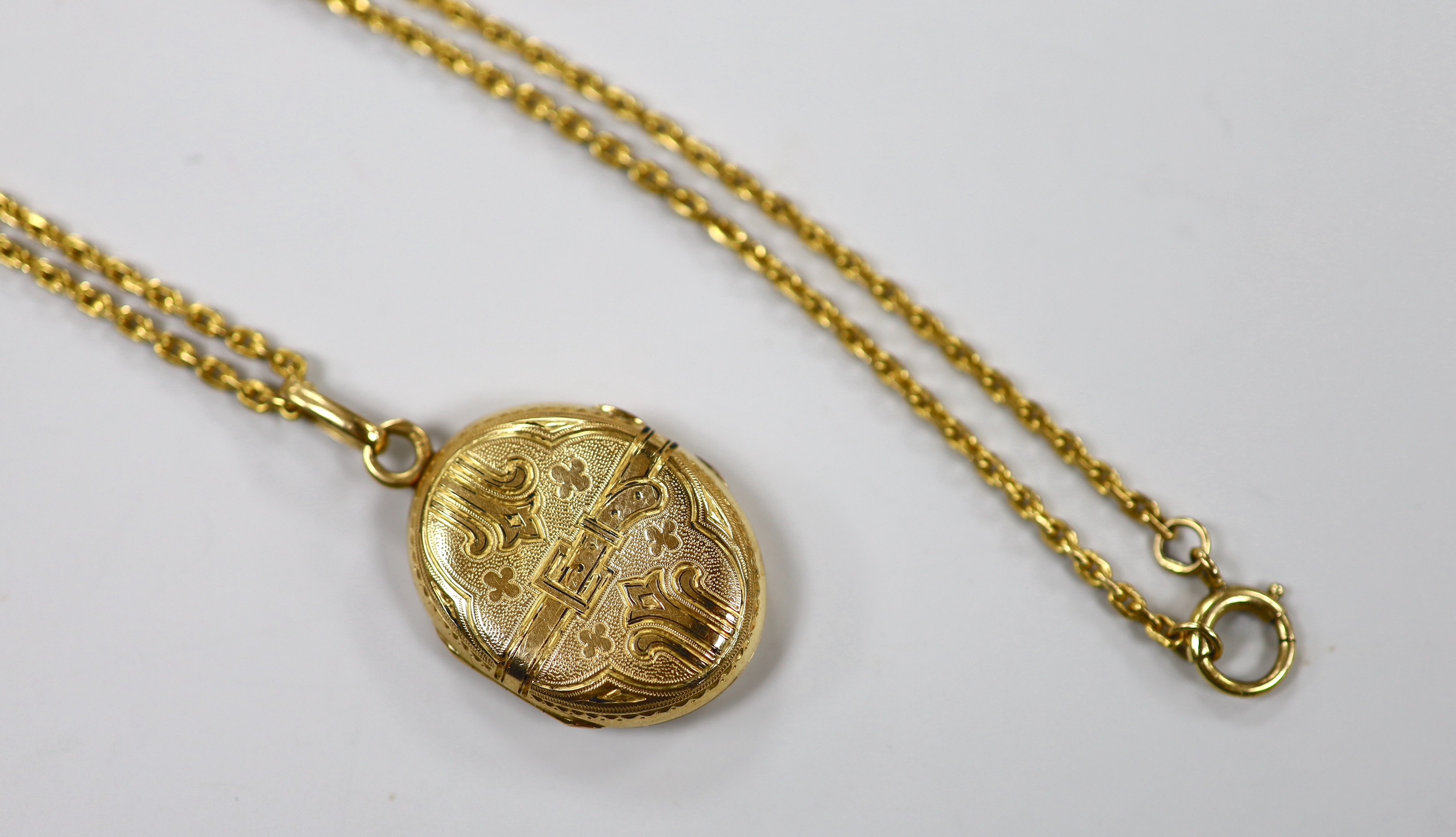 A continental engraved yellow metal oval locket, overall 38mm, on a 9ct chain, 47cm, gross weight 18.9 grams.